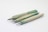 Three wooden mechanical pencils are arranged diagonally on a plain white background. The pencils have a natural greenish tint, with metallic tips and ends. Each pencil displays a unique shade and wood grain pattern, adding a rustic and artisanal appearance.