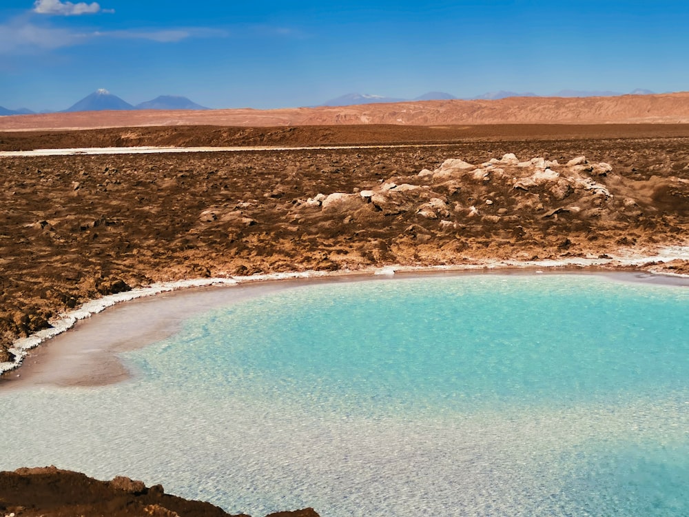 a body of water with a rocky beach and mountains in the background