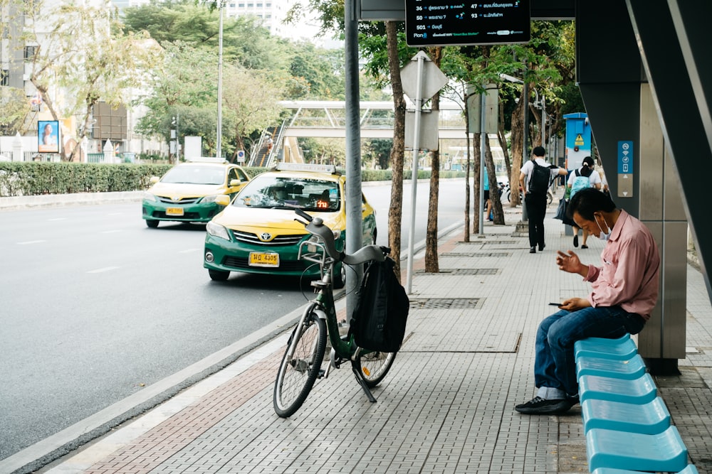 a person sitting on a sidewalk next to a bicycle and a person on a phone