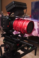 A professional camera setup with a distinct red lens marked 18-35, mounted on a rig. The camera has various control buttons and a matte box attached. It is set up in an indoor environment on a table or platform.