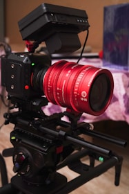 A professional camera setup with a distinct red lens marked 18-35, mounted on a rig. The camera has various control buttons and a matte box attached. It is set up in an indoor environment on a table or platform.