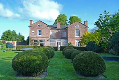 a large brick house with a lawn and hedges in front of it with Moseley Old Hall in the background