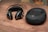 A pair of black, over-ear headphones with silver accents lies on a wooden surface next to a matching black zippered carrying case. The headphones have a sleek, modern design, and the case has a logo embossed on its top.