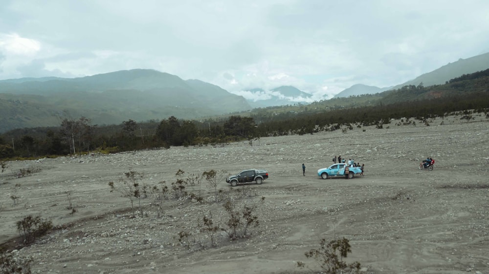 um grupo de carros dirigindo em uma estrada de terra com montanhas ao fundo