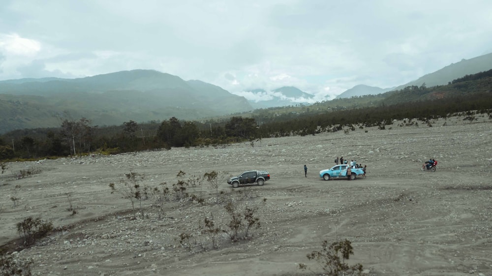 a group of cars driving on a dirt road with mountains in the background