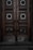 An ornate double door crafted from dark wood features intricate metalwork details. The panels are adorned with circular wrought iron inserts, each with unique, decorative symbols. The door handles are also made of metal, finely detailed in design. The surface of the doors shows signs of wear, lending an aged and historical appearance.