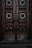An ornate double door crafted from dark wood features intricate metalwork details. The panels are adorned with circular wrought iron inserts, each with unique, decorative symbols. The door handles are also made of metal, finely detailed in design. The surface of the doors shows signs of wear, lending an aged and historical appearance.