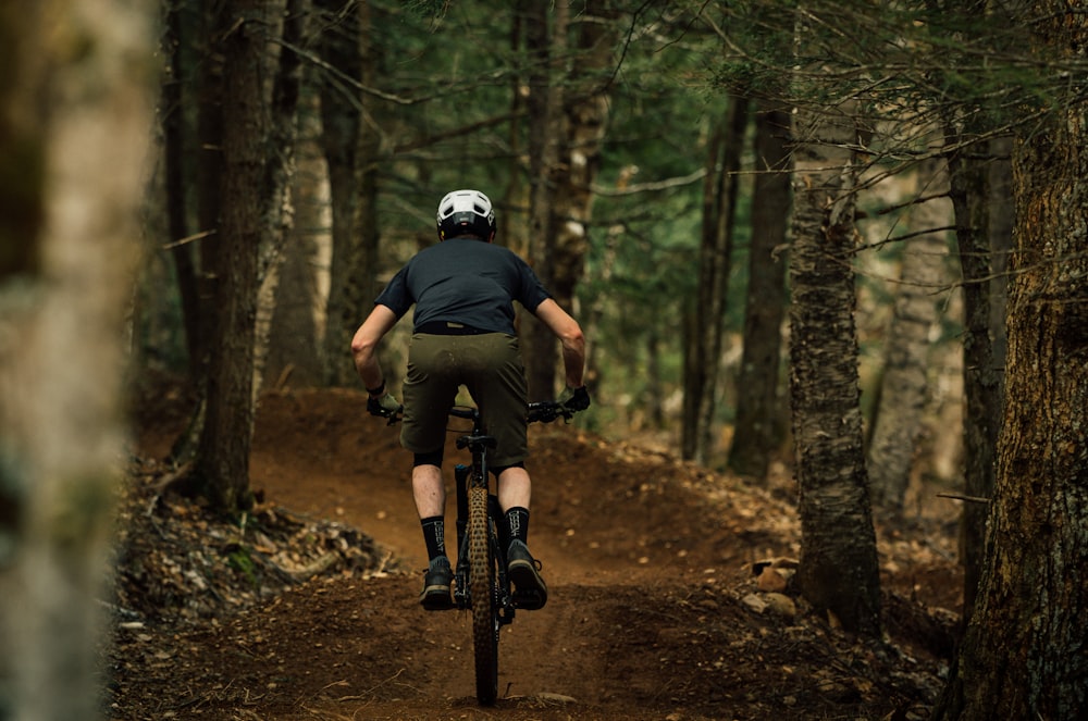 a man riding a bike down a dirt road in a forest