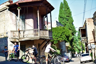 A sunlit street scene from the 1990s with kids riding BMX bikes and a classic car parked nearby.