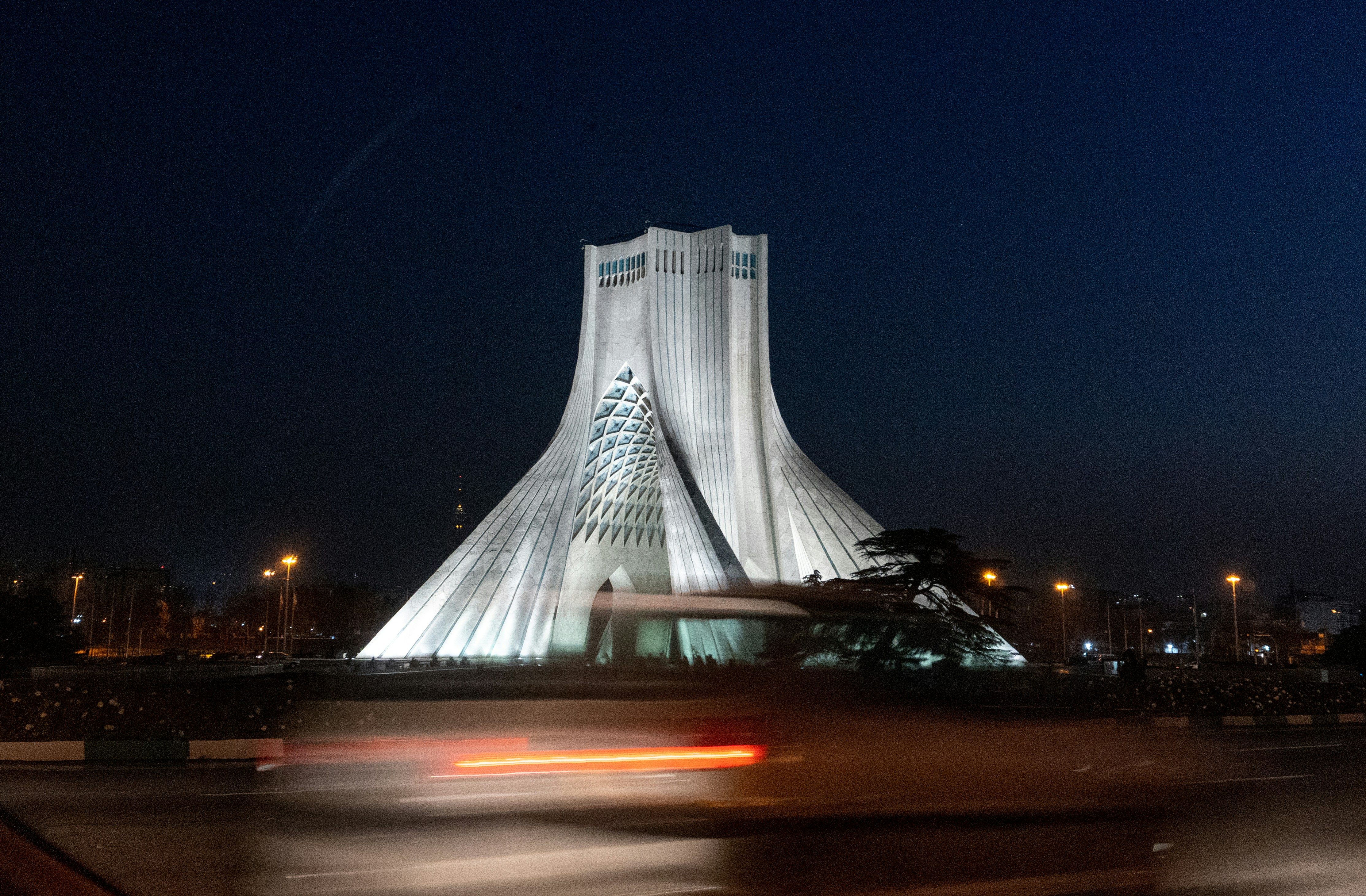 um grande edifício em forma de pirâmide com a torre de Azadi no fundo