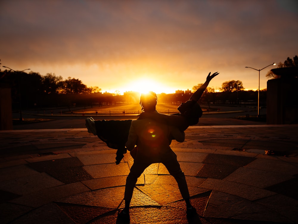 Una estatua de una persona sosteniendo un arma frente a una puesta de sol