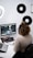 A person with curly hair wearing headphones is sitting at a desk, focused on editing video content on a computer. The desk is equipped with various gadgets, including a laptop and other tech accessories. The room's wall displays vinyl records, adding an artistic touch.
