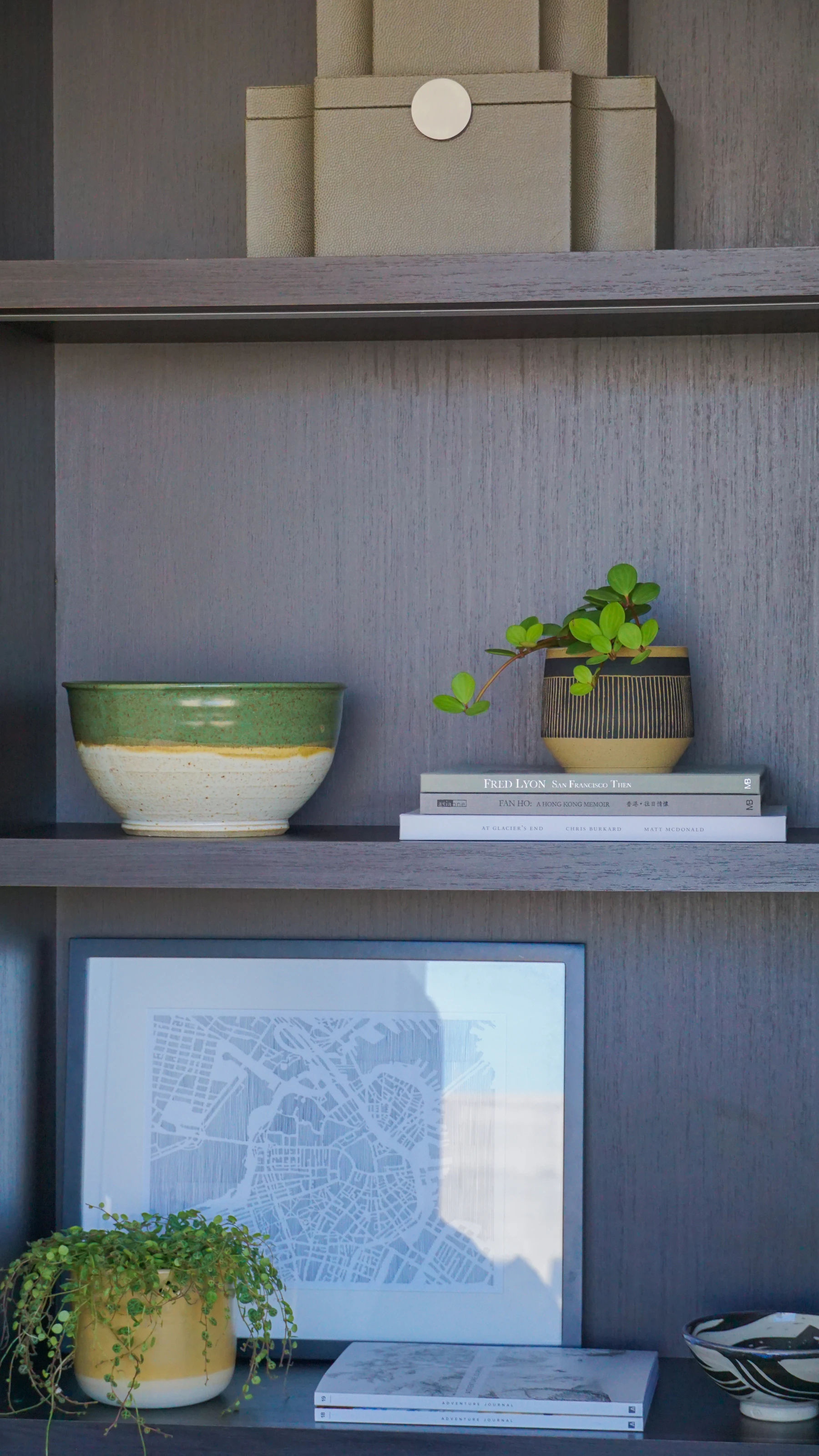A gray shelf holding a green glazed bowl, a striped planter and a short stack of books