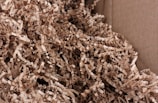 A close-up view of crinkled brown paper strips filling a cardboard box. The paper strips are densely packed and create a textured and layered appearance.