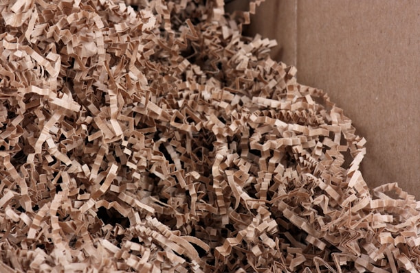 A close-up view of crinkled brown paper strips filling a cardboard box. The paper strips are densely packed and create a textured and layered appearance.