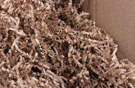 A close-up view of crinkled brown paper strips filling a cardboard box. The paper strips are densely packed and create a textured and layered appearance.