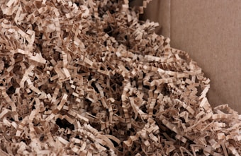 A close-up view of crinkled brown paper strips filling a cardboard box. The paper strips are densely packed and create a textured and layered appearance.