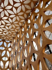 A complex architectural design featuring a geometric pattern of interconnected circular and triangular shapes. The structure is composed of wooden elements and large windows that allow natural light to filter through.