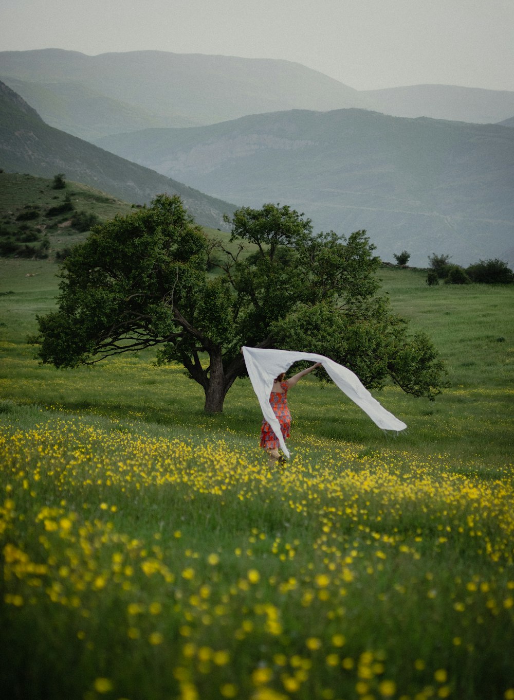 a person jumping in a field of flowers with a tree in the background