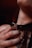 A hand is gently resting on a person's neck, where a black leather collar with metal details is worn. The collar features a decorative heart-shaped design. The lighting is dim and warm, creating a sense of intimacy.