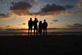 a group of people standing on a beach at sunset