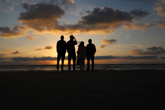 a group of people standing on a beach at sunset