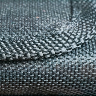 A close-up view of a woven fabric showcasing a detailed pattern and texture with tightly interlaced fibers. The image focuses on the intersection of different textile strands, highlighting the intricate craftsmanship.