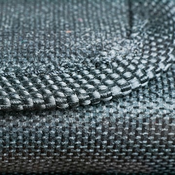 A close-up view of a woven fabric showcasing a detailed pattern and texture with tightly interlaced fibers. The image focuses on the intersection of different textile strands, highlighting the intricate craftsmanship.