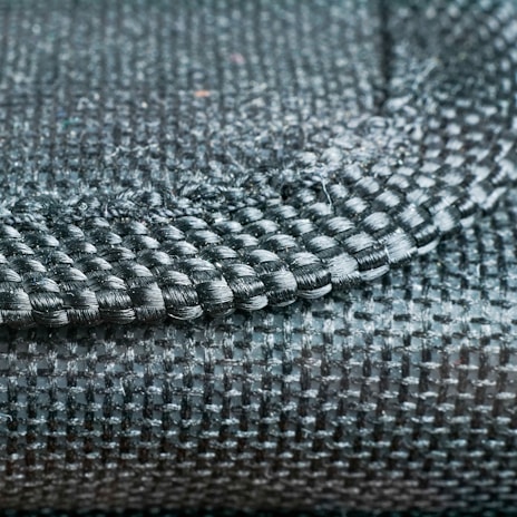 A close-up view of a woven fabric showcasing a detailed pattern and texture with tightly interlaced fibers. The image focuses on the intersection of different textile strands, highlighting the intricate craftsmanship.