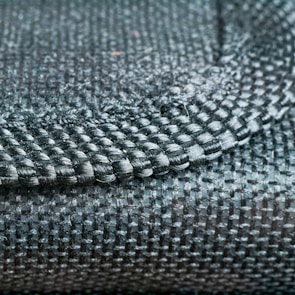 A close-up view of a woven fabric showcasing a detailed pattern and texture with tightly interlaced fibers. The image focuses on the intersection of different textile strands, highlighting the intricate craftsmanship.