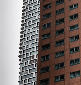 A close-up view of two adjacent skyscrapers, one with a modern white and glass facade and the other with a reddish-brown brick exterior. The buildings have numerous windows and exhibit contrasting architectural styles.