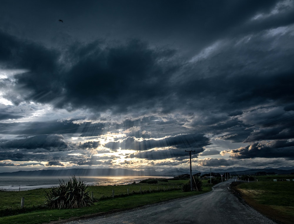 a road with grass and a cloudy sky