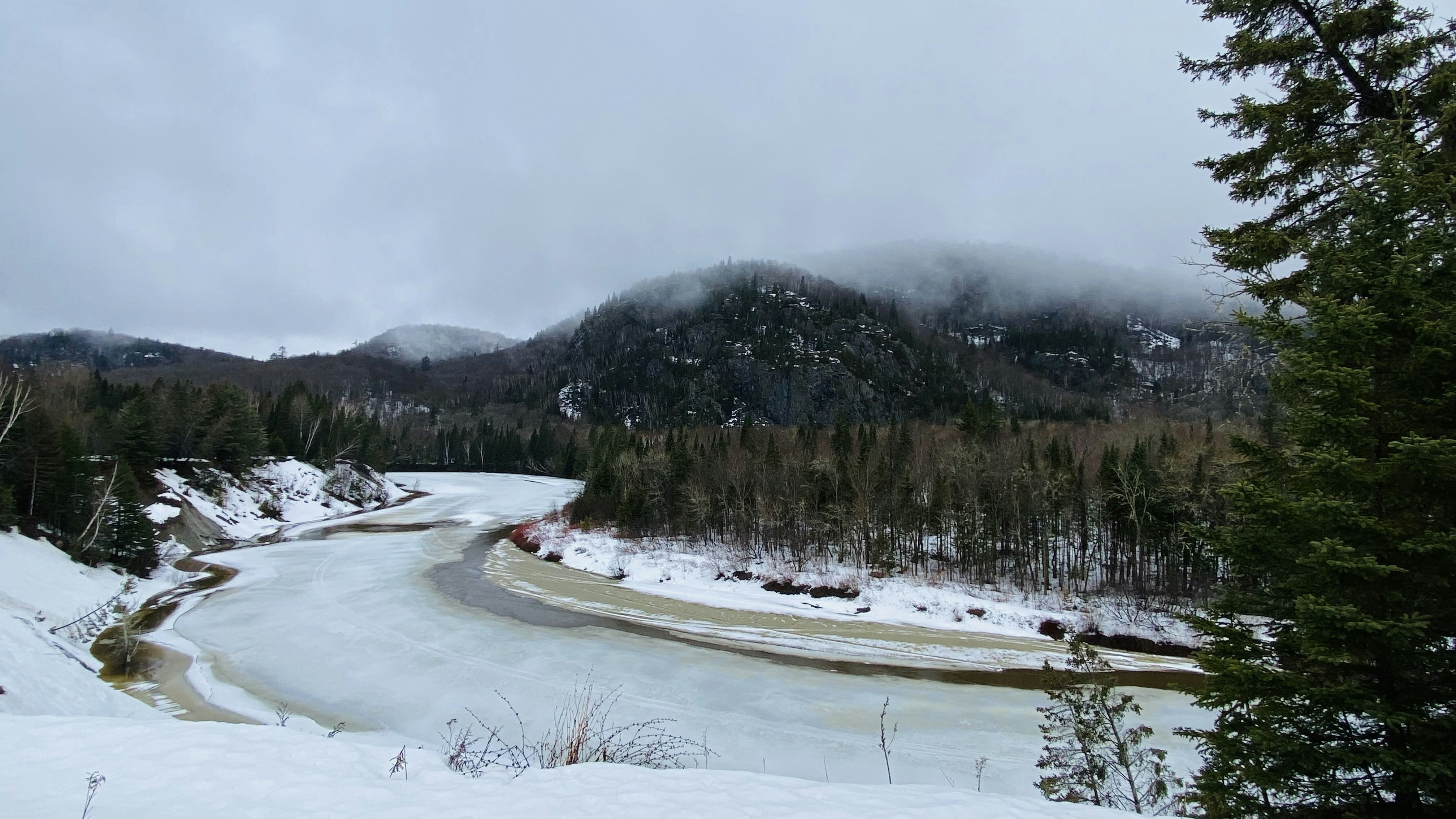 Snow-covered river valley surrounded by evergreen trees in the Canadian Rockies during early autumn.