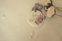 A decorative tag with the words 'for Jesus' written on it, adorned with pastel-colored flowers and a ribbon, lies on a light surface next to a bunch of soft pink roses.
