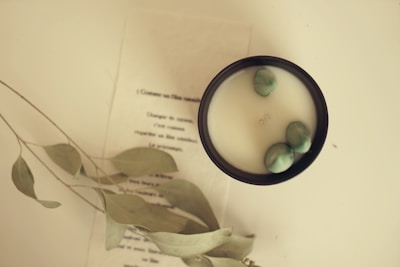Close-up of a black candle surrounded by green leaves and crystals on a white surface.