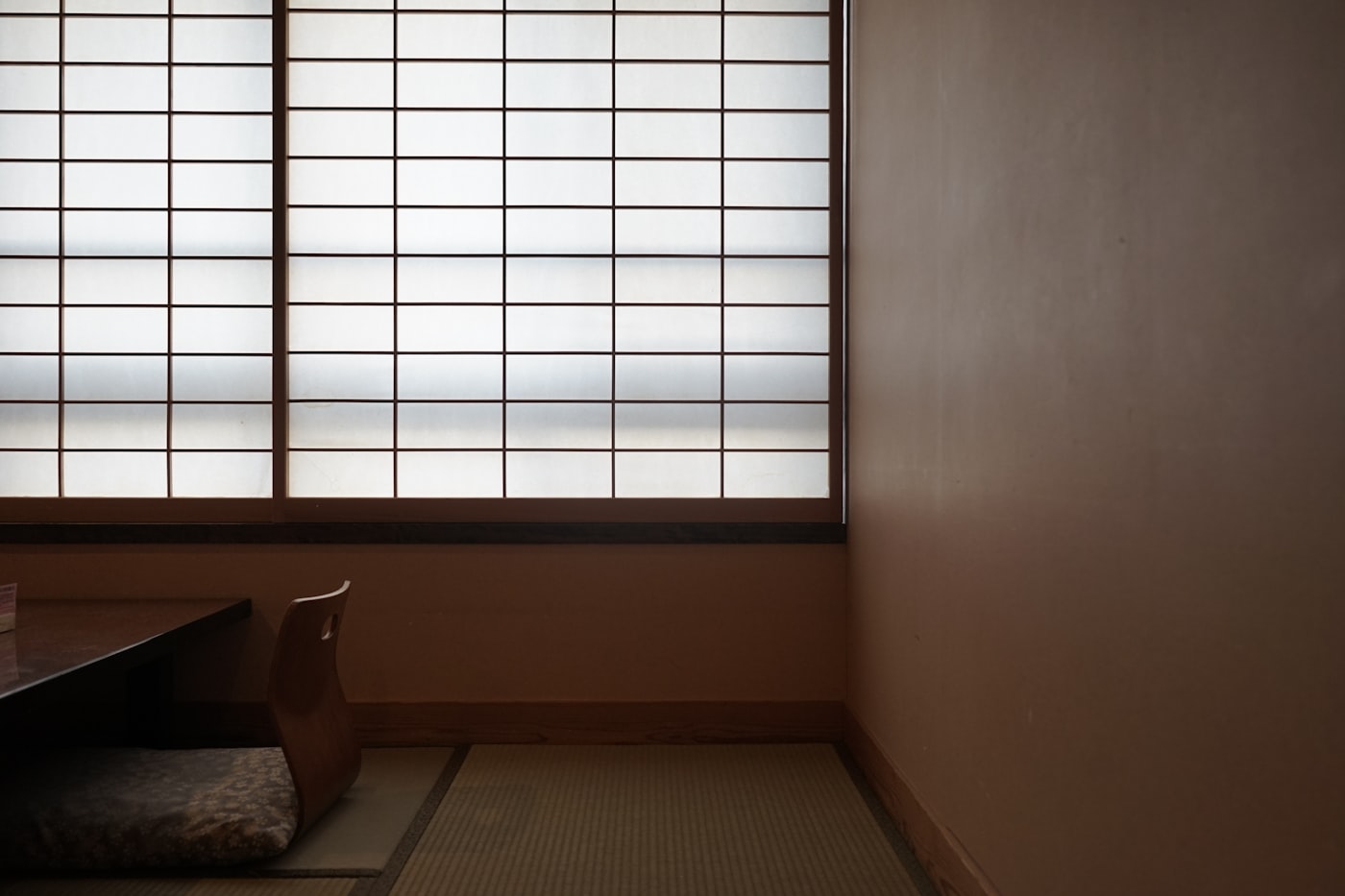 Traditional Japanese tatami room with shoji paper screens, a low wood backless chair, and tan plaster walls, the inspiration for modern japandi