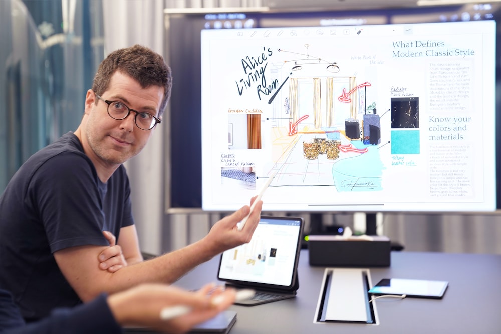 a man sitting at a desk with a laptop and a white board