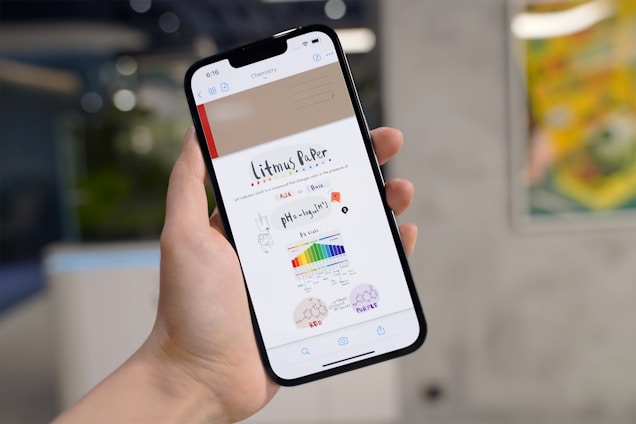 A person holds a smartphone showing a digital note about litmus paper. The note includes diagrams and a pH scale with various colors, along with some text and drawings of a brain and test tube.