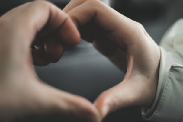 Two hands forming a heart shape against a blurred background.