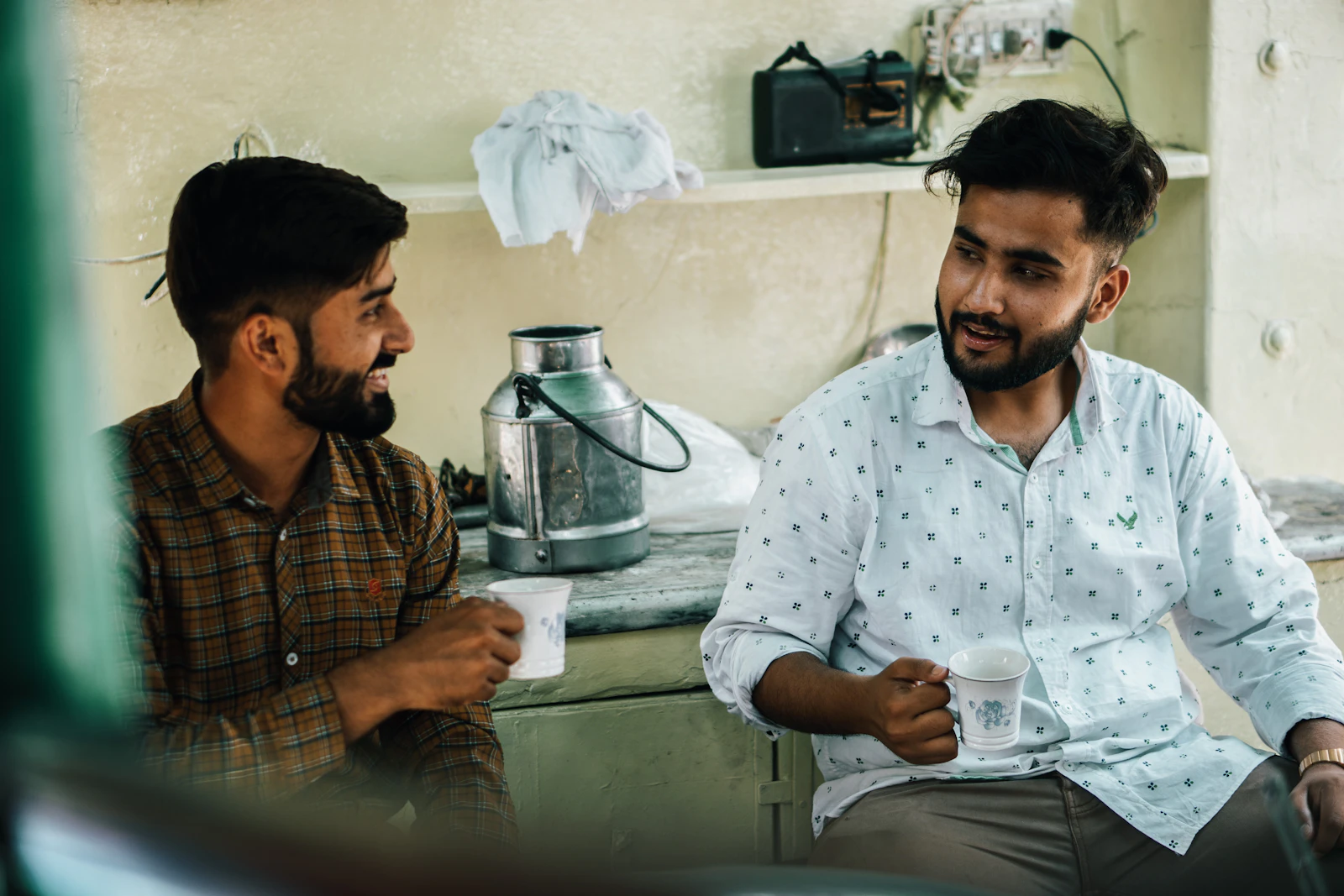 Two people sitting together in a kitchen having a relaxed conversation, representing the end-of-stay handover between the respite worker and the household