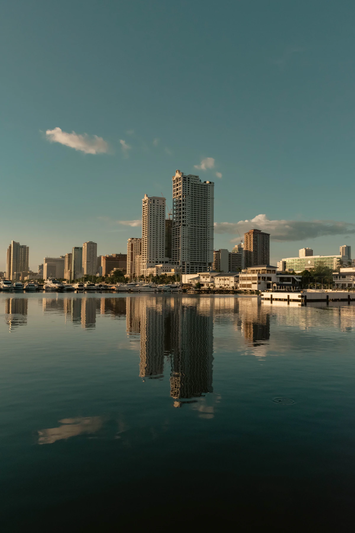 Manila high-rise buildings reflected in calm water at a marina in late-afternoon light
