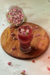 Close-up of a glass of rose lassi with frothy top and rose petals sprinkled.