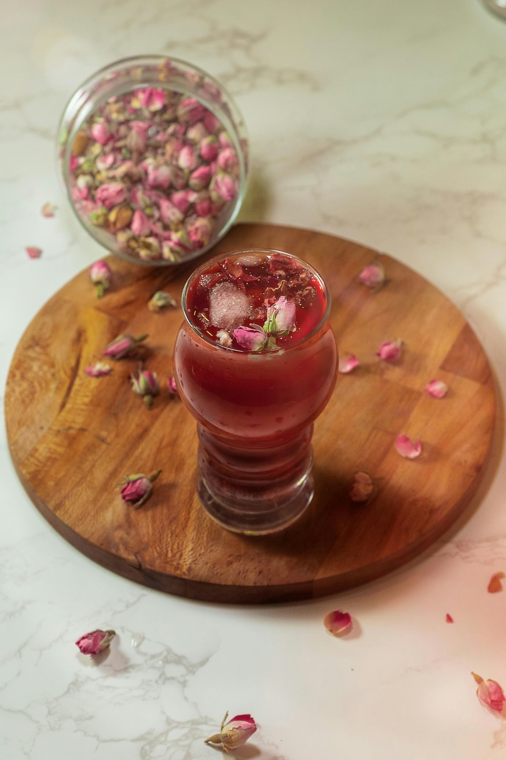 a glass of red liquid with a pink substance on a wooden surface