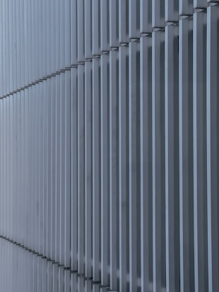 Vertical metallic slats arranged in a repetitive pattern create a symmetrical and minimalist appearance. The structure appears to be part of an architectural facade, showcasing straight lines and a modern design.