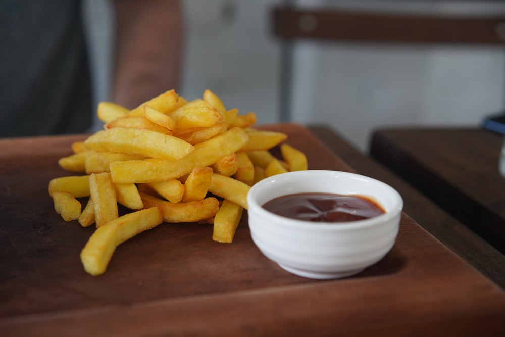 a bowl of french fries and sauce on a wooden table