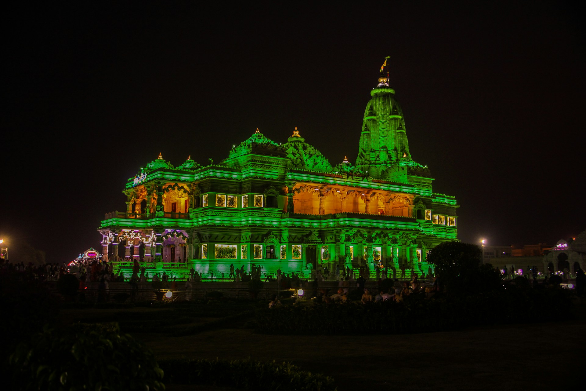 Evening view of Maha Lakshmi Mandir glowing warmly under soft lights, with devotees gathered peacefully.