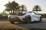 Elegant sports car parked on a palm-lined beach road with white sand and blue skies.