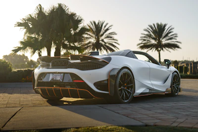 Elegant sports car parked on a palm-lined beach road with white sand and blue skies.