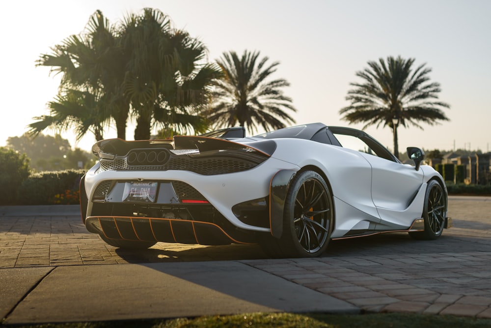 a white sports car parked on a brick road with palm trees