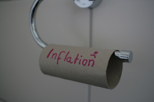 An empty toilet paper roll hangs on a dispenser, with the word 'Inflation' written in red on the cardboard tube.